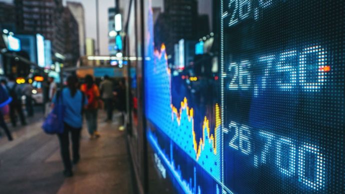 Een scherm met daarop een index van een aandelenbeurs, met mensen op de achtergrond.