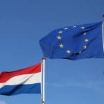 Een foto van de vlag van de Europese Unie (EU), met daarnaast de vlag van Nederland, en op de achtergrond een blauw lucht