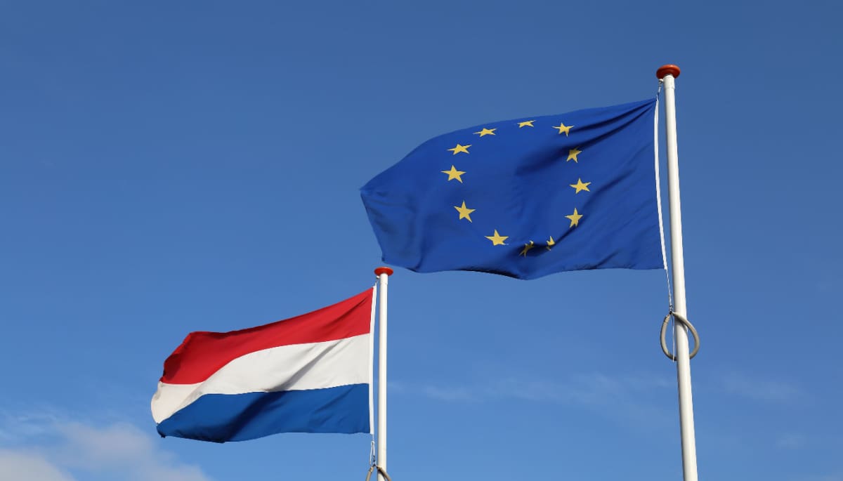 Een foto van de vlag van de Europese Unie (EU), met daarnaast de vlag van Nederland, en op de achtergrond een blauw lucht