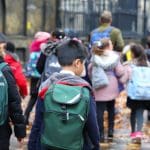 Een afbeelding van een groep schoolkinderen op een rijtje, met een docent_leraar die de stoet begeleidt
