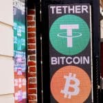 Een uithangbord en -scherm in een drukke straat met daarop twee grote cryptomunten_ Tether (USDT) en bitcoin (BTC)