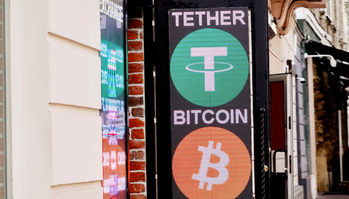 Een uithangbord en -scherm in een drukke straat met daarop twee grote cryptomunten_ Tether (USDT) en bitcoin (BTC)