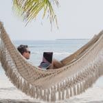 foto van een man in een hangmat op het strand met een laptop