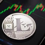 Een afbeelding van een litecoin (LTC) munt op een mobiele telefoon met een grafiek op een crypto exchange