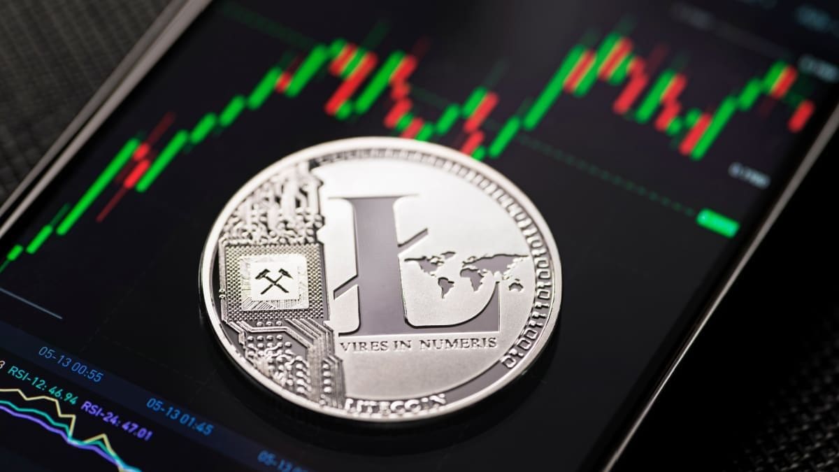 Een afbeelding van een litecoin (LTC) munt op een mobiele telefoon met een grafiek op een crypto exchange