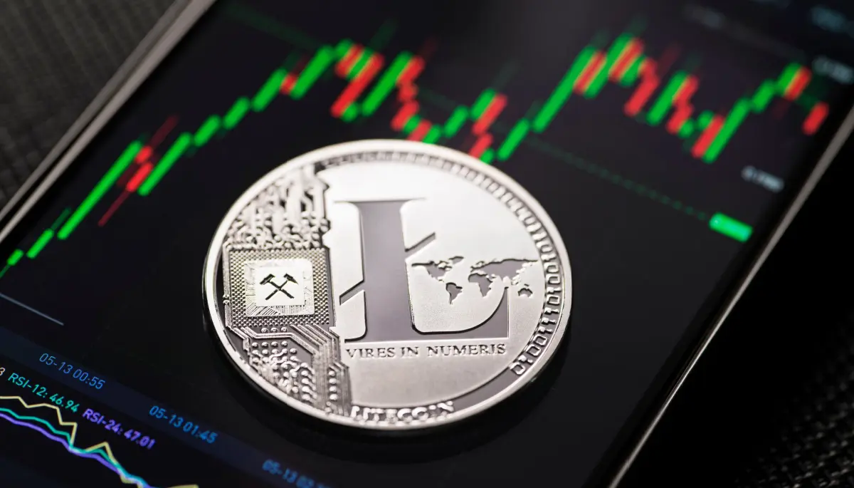 Een afbeelding van een litecoin (LTC) munt op een mobiele telefoon met een grafiek op een crypto exchange