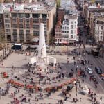 Een afbeelding van het plein van de Dam in Amsterdam, met daarbij het monument en een hoop Nederlanders