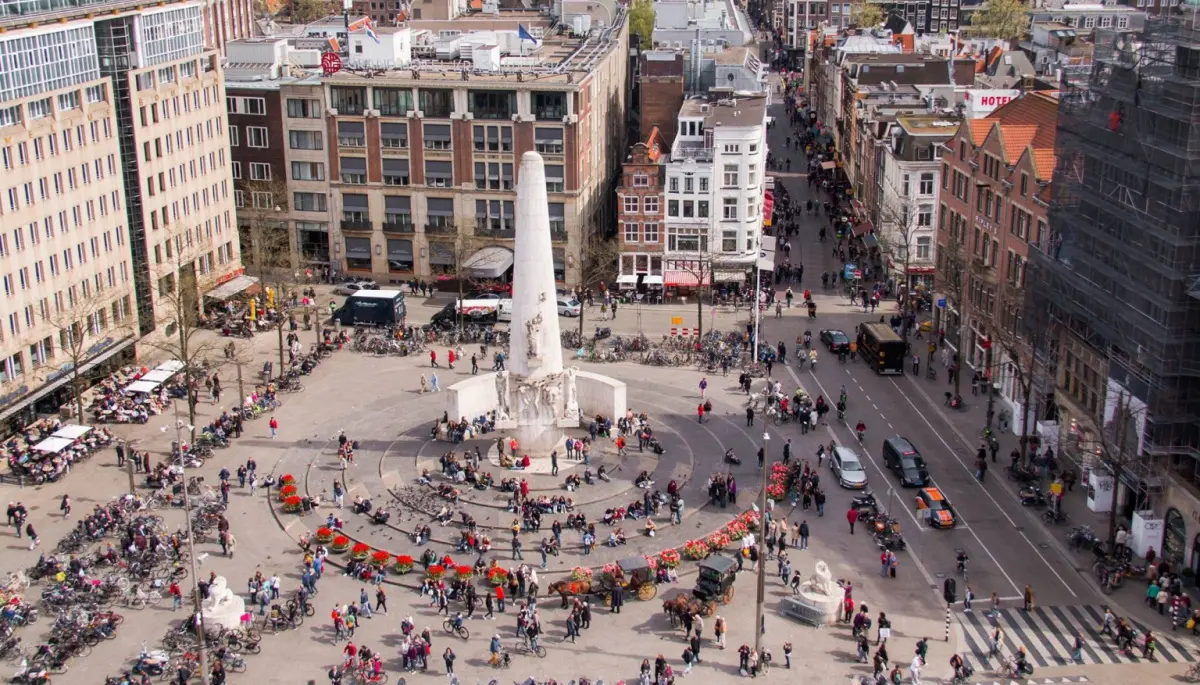 Een afbeelding van het plein van de Dam in Amsterdam, met daarbij het monument en een hoop Nederlanders