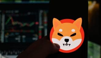Het logo van de memecoin shiba inu (SHIB) op een mobiele telefoon met op de achtergrond een koers in candle chart format, op een cryptobeurs
