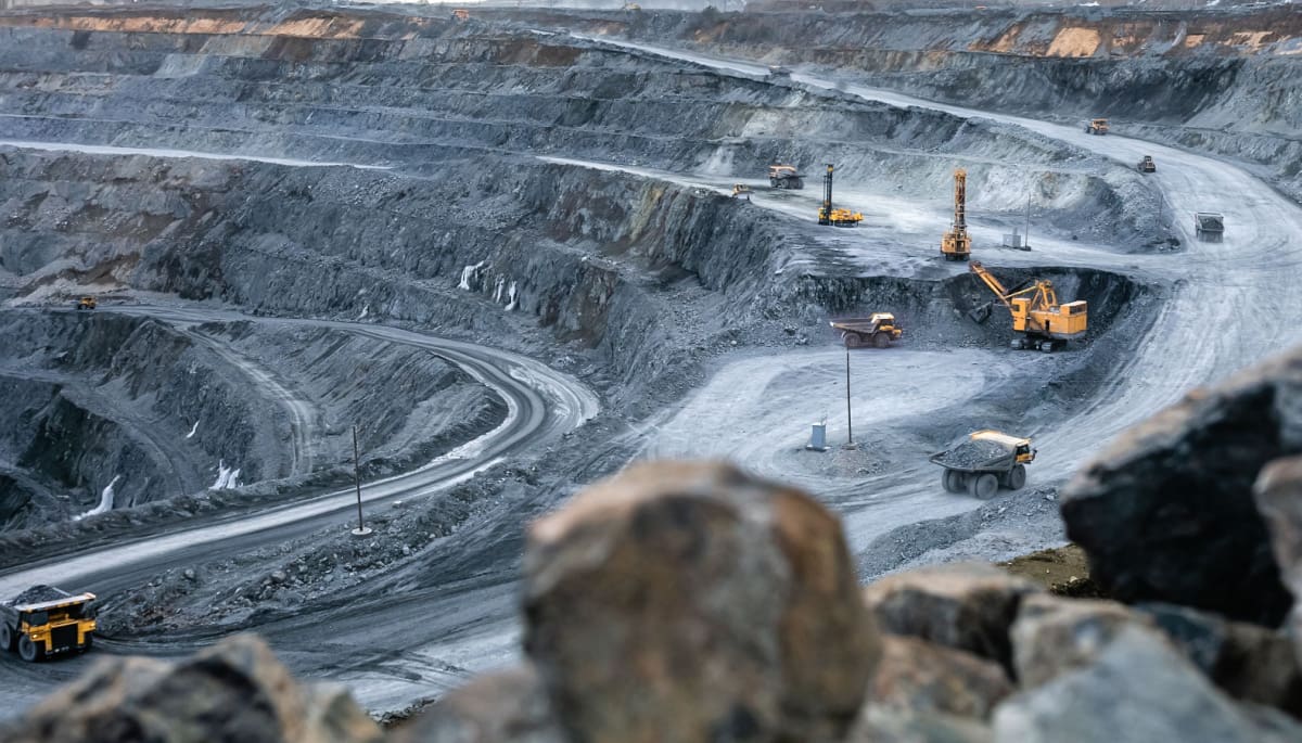 Een afbeelding van een grote mijnbouwput, waar een mijnbouwbedrijf bezig is met het delven van metalen en andere fysieke grondstoffen
