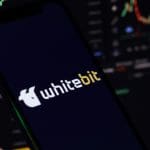 Een afbeelding van whitebit, een cryptomunt afkomstig van een grote crypto exchange. Het logo van whitebit staat op een mobiel, en op de achtergrond staan grafieken