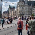 Een afbeelding van een lopende menigte Nederlanders en toeristen in Amsterdam, met een tramrails ertussen