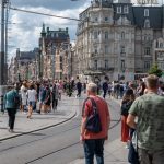 Een afbeelding van een lopende menigte Nederlanders en toeristen in Amsterdam, met een tramrails ertussen