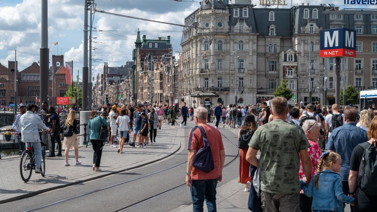 Een afbeelding van een lopende menigte Nederlanders en toeristen in Amsterdam, met een tramrails ertussen