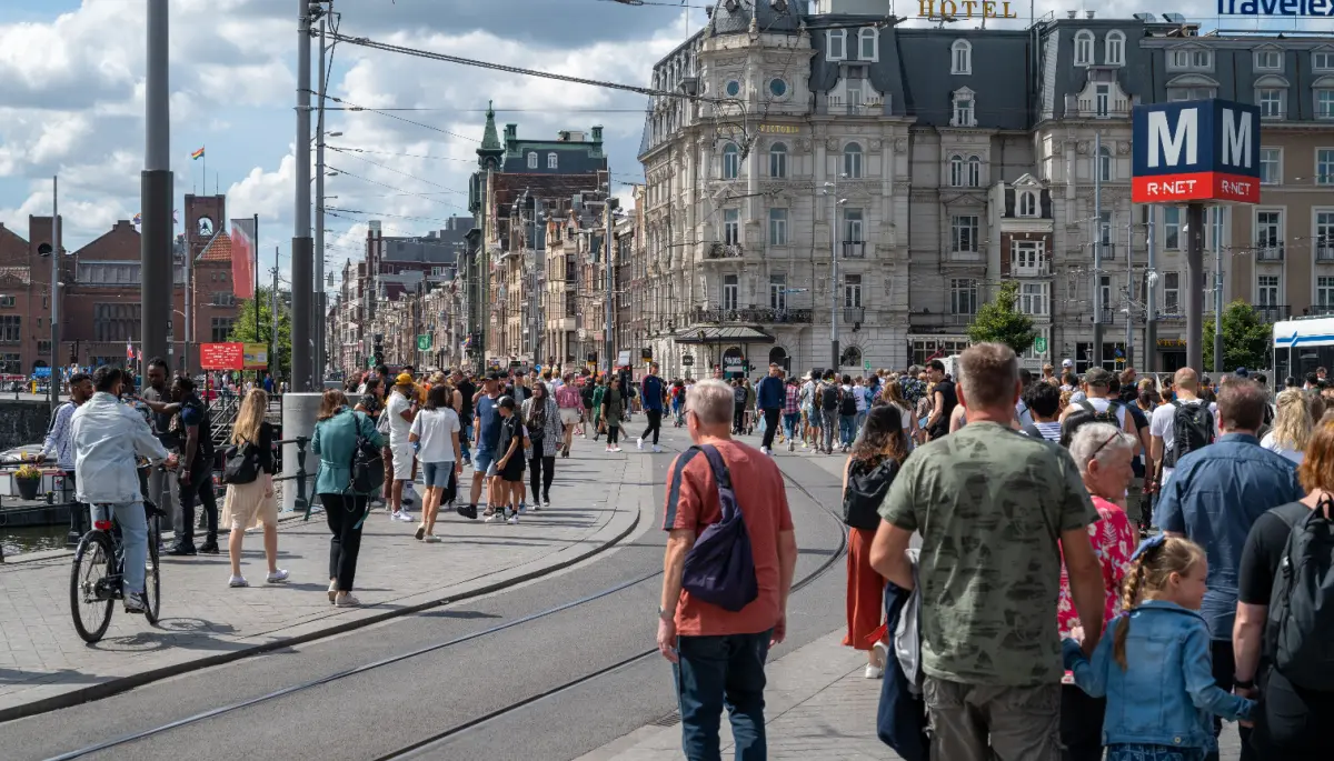 Een afbeelding van een lopende menigte Nederlanders en toeristen in Amsterdam, met een tramrails ertussen