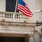 Een afbeelding van de aandelenbeurs van New York, met daarbij een straatbordje met Wall Street