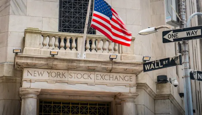 Een afbeelding van de aandelenbeurs van New York, met daarbij een straatbordje met Wall Street