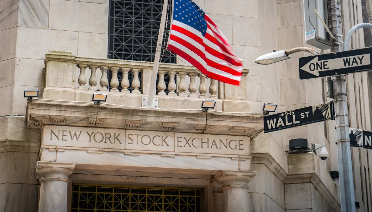 Een afbeelding van de aandelenbeurs van New York, met daarbij een straatbordje met Wall Street
