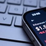 Een afbeelding van een lage, rode ethereum (ETH) koers op een mobiele telefoon bij een toetsenbord
