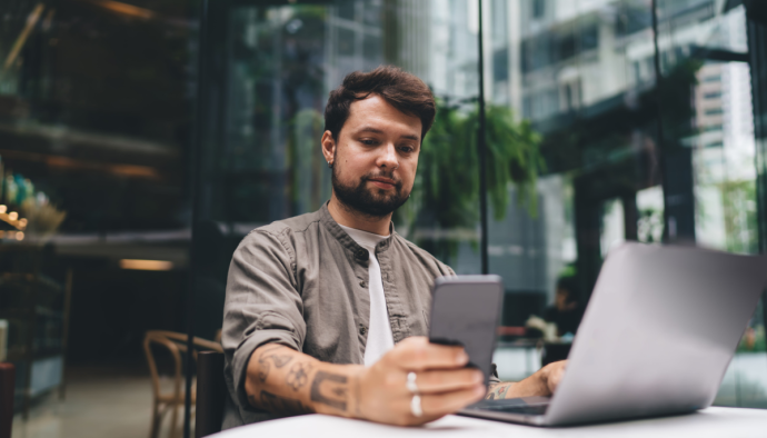 Man kijkt naar mobiel achter latop