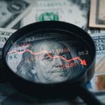 Een afbeelding van een Amerikaanse dollar en een vergrootglas met daarin een dalende rode koers met cijfers