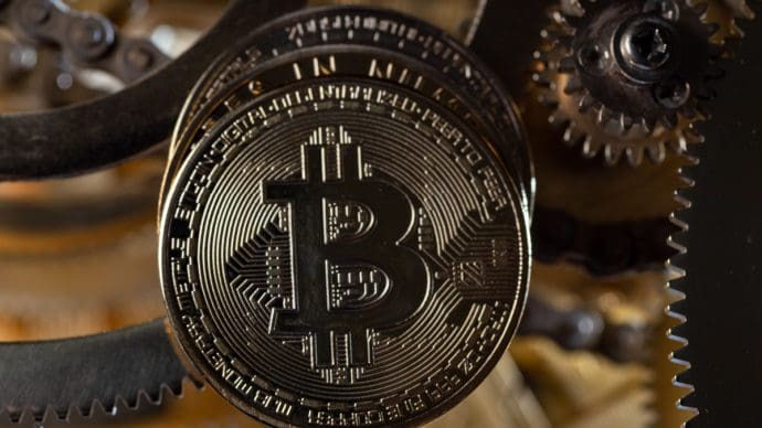 Een afbeelding van een bitcoin (BTC) munt bij een aantal gouden tandwielen