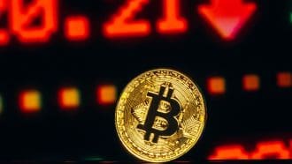 Een afbeelding van een bitcoin (BTC) munt met rode cijfers en een dalende prijs op de achtergrond