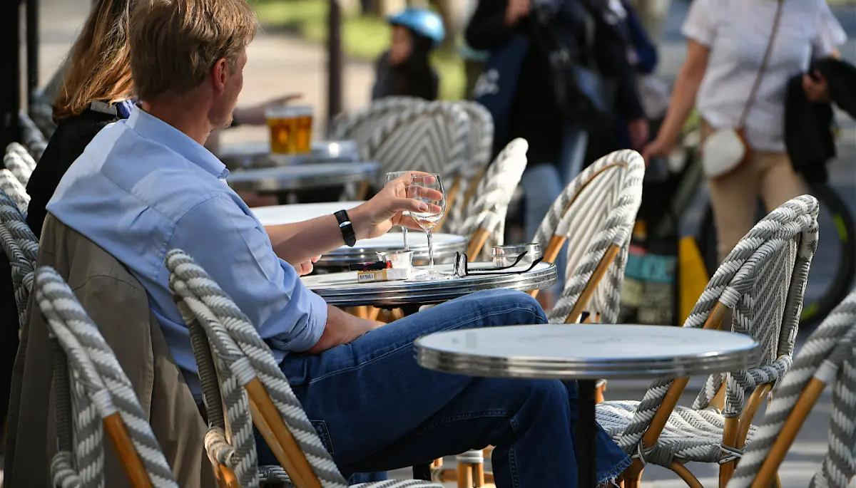 Een afbeelding van een man in Parijs die op een terras loopt uit te rusten met een drankje erbij