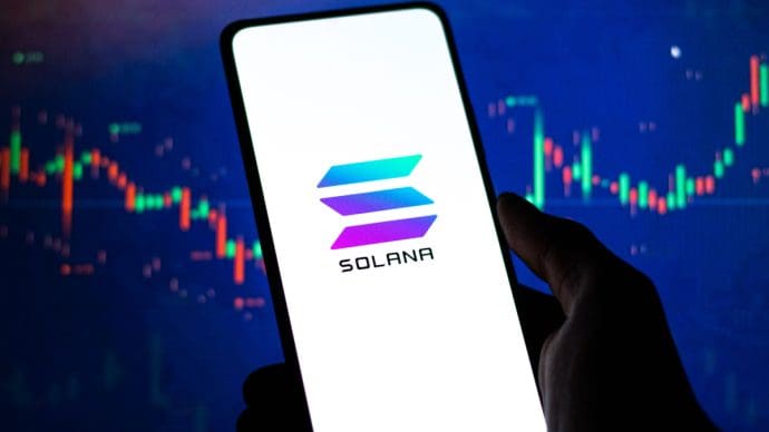 Een afbeelding van een mobiele telefoon met het Solana (SOL) logo op de voorkant en op de achtergrond een stijgende grafiek van een koers van een crypto