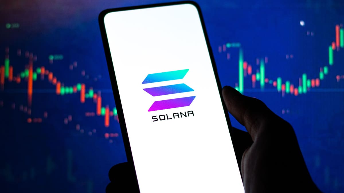 Een afbeelding van een mobiele telefoon met het Solana (SOL) logo op de voorkant en op de achtergrond een stijgende grafiek van een koers van een crypto