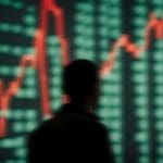 Een afbeelding van een scherm met stijgende koersen van crypto of aandelen voor het silhouet van een handelaar