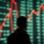Een afbeelding van een scherm met stijgende koersen van crypto of aandelen voor het silhouet van een handelaar