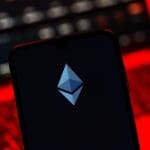 Een afbeelding van het Ethereum (ETH) logo met op de achtergrond een laptop met rode alarmerende kleuren en crypto pagina's