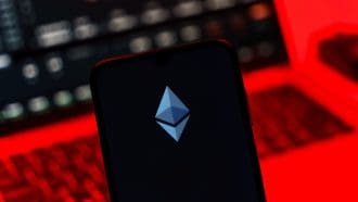 Een afbeelding van het Ethereum (ETH) logo met op de achtergrond een laptop met rode alarmerende kleuren en crypto pagina's