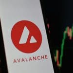 Een afbeelding van het logo van cryptomunt Avalanche (AVAX) met op de achtergrond een koersgrafiek