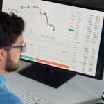 Een crypto handelaar die een koers en grafiek aan het analyseren is op zijn laptop en computer