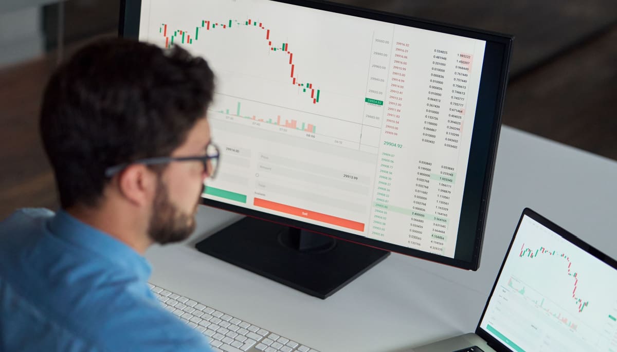 Een crypto handelaar die een koers en grafiek aan het analyseren is op zijn laptop en computer