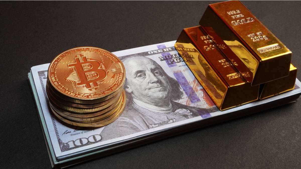 Een afbeelding van een aantal bitcoin munten op een stapeltje dollars met daarbij een aantal goudstaven