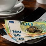 Een afbeelding van een bakje met fooi, waar enkele biljetten van 100, 50 en 20 euro liggen met wat euromunten