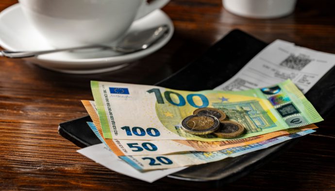 Een afbeelding van een bakje met fooi, waar enkele biljetten van 100, 50 en 20 euro liggen met wat euromunten