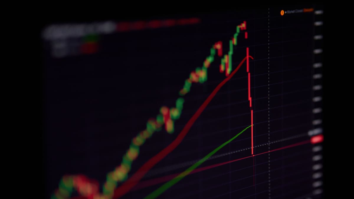 Een afbeelding van een flash crash van een aandeel of crypto koers, met een harde rode lijn direct naar beneden van een candle chart