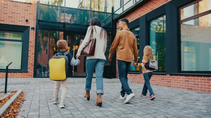 Een afbeelding van een gezin met twee kinderen dat naar een school toe loopt