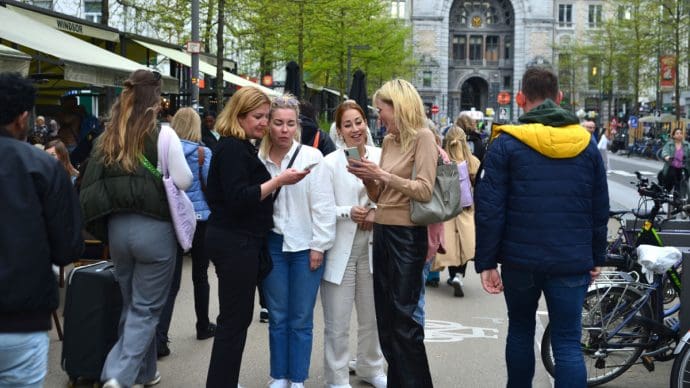 Een afbeelding van een paar vrouwen die hun mobiel bekijken op een drukke plek in Antwerpen