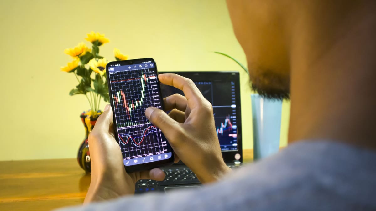 Een afbeelding van een stijgende crypto koers op een mobiele telefoon die door een amateur handelaar wordt vastgehouden