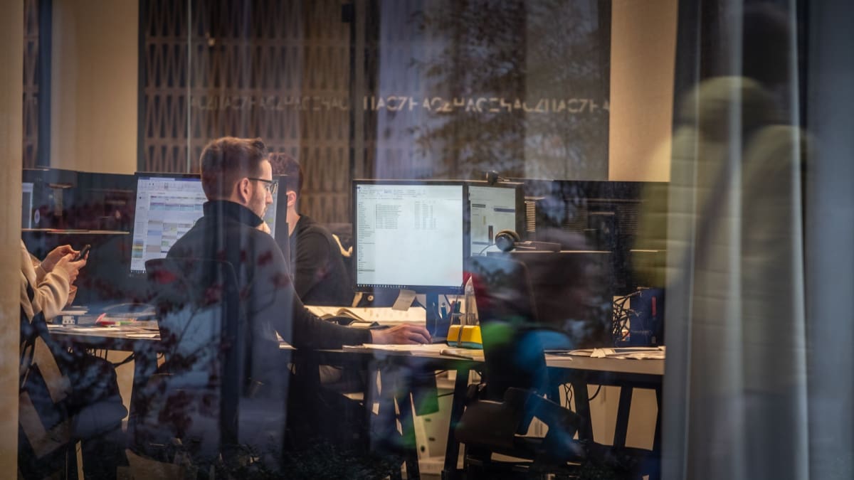 Een afbeelding van een werknemer die werkt op een druk kantoor, gefotografeerd van buitenaf