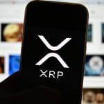Een afbeelding van het XRP logo op een mobiele telefoon met op de achtergrond media gerelateerd aan Ripple en hun munt XRP
