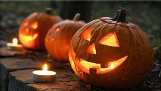 Een afbeelding van verlichte pompoenen waar enge gezichten in gesneden zijn voor Halloween