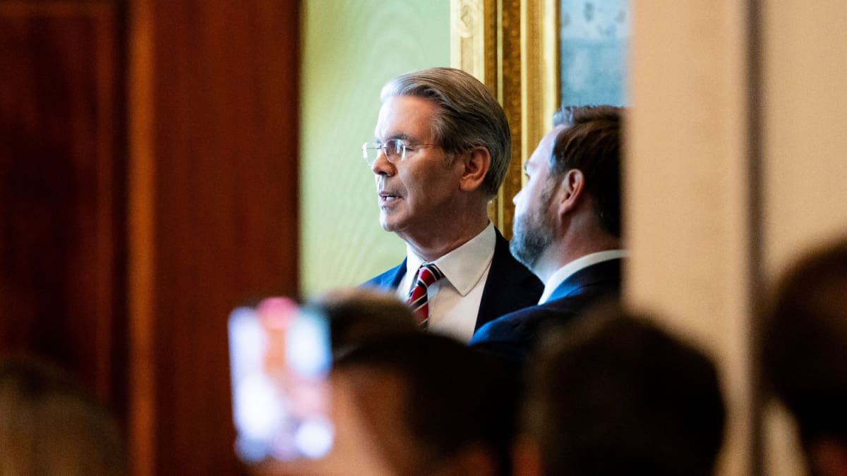 De Amerikaanse president van Financiën, Scott Bessent, te zien in het Witte Huis door een kier in gesprek met JD Vance