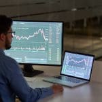 Een afbeelding van een actieve belegger die met twee schermen een bepaalde koers van een aandeel of crypto aan het analyseren is