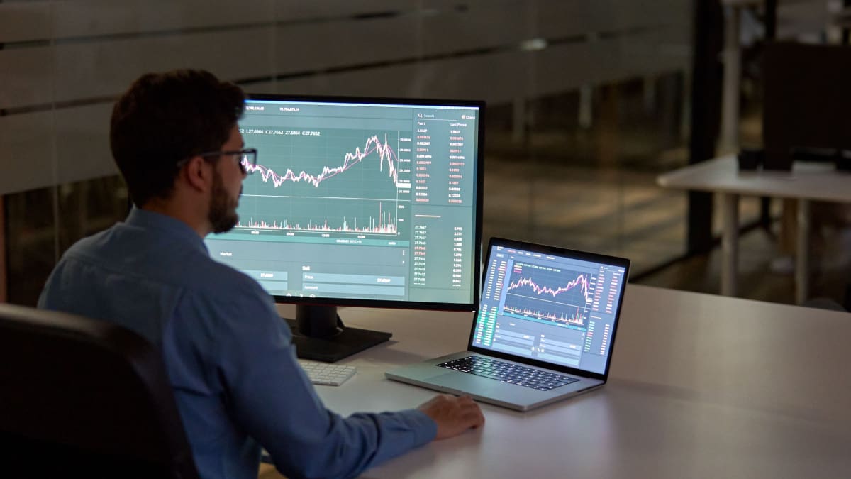 Een afbeelding van een actieve belegger die met twee schermen een bepaalde koers van een aandeel of crypto aan het analyseren is